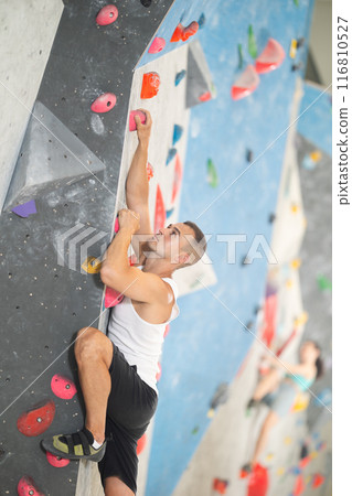 Young man climbing on artificial rock wall in rock-climbing gym 116810527