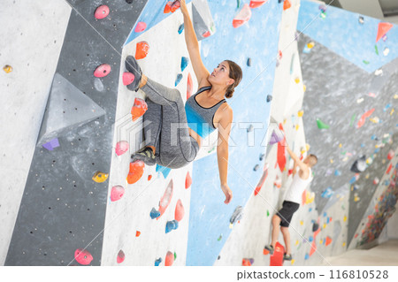 Young girl climbing on artificial rock wall in rock-climbing gym 116810528