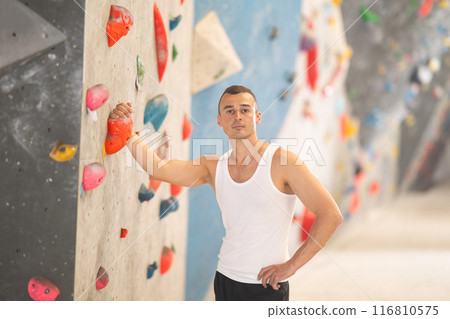 Young male climber posing at artificial rock wall in climbing hangar 116810575