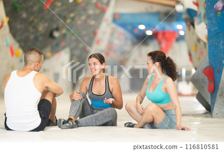 Three climbing friends sit on the floor and discuss options for climbing climbing wall. Share their impressions Three climbing friends sit on the floor and discuss options for climbing climbing wall. Share their impressions 116810581