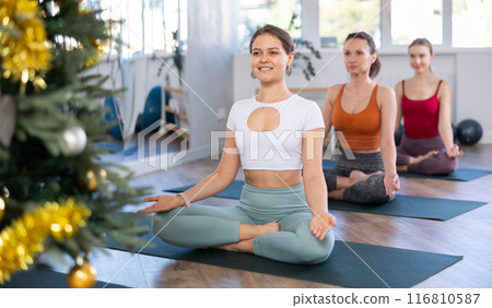 Girls making yoga meditation in lotus pose in modern fitness studio during christmas celebration Girls making yoga meditation in lotus pose in modern fitness studio during christmas celebration 116810587