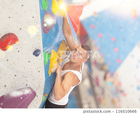 Young man climbing on artificial rock wall in rock-climbing gym Young man climbing on artificial rock wall in rock-climbing gym 116810666
