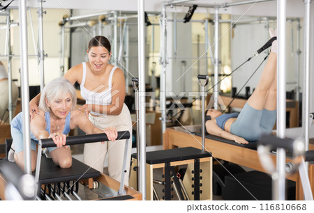 Elderly woman exercising on reformer with young female instructor 116810668