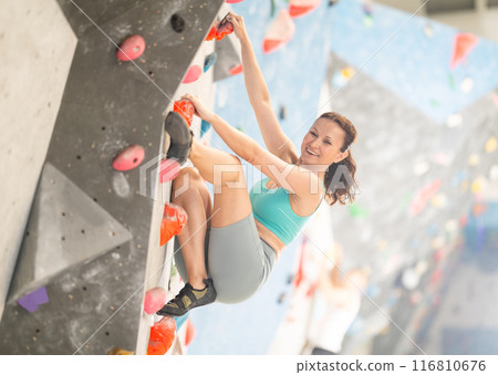 Middle-aged woman climbing on artificial rock wall in rock-climbing gym 116810676