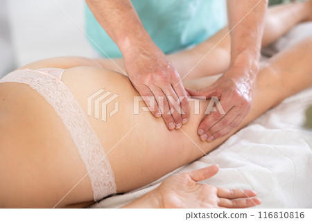 Woman covered with white towel lies and enjoys during anti-cellulite massage in hips and legs 116810816