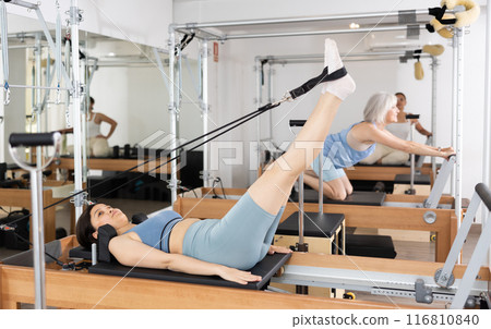 Woman exercising torson rotation at sport gym using pilates reformer beds Woman exercising torson rotation at sport gym using pilates reformer beds 116810840