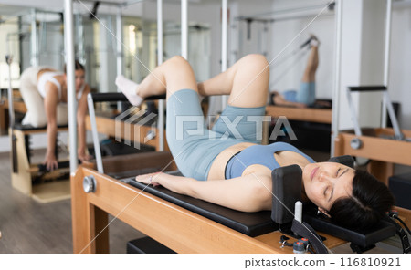 Positive woman doing lower back exercises while lying on Pilates bed in wellness center 116810921