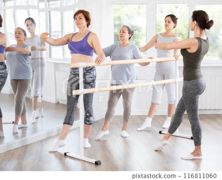 Woman mastering battement tendu with group of beginners and choreographer 116811060