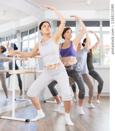 Woman practicing demi plie at barre in amateur ballet class Woman practicing demi plie at barre in amateur ballet class 116811090