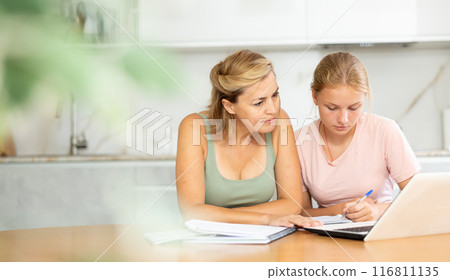 Woman offering assistance to teenage daughter studying at home 116811135