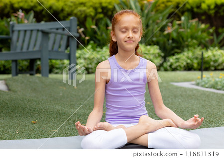 Biracial girl practices yoga in garden, sitting cross-legged with copy space Biracial girl practices yoga in garden, sitting cross-legged with copy space 116811319