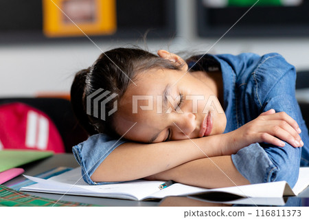 Tired biracial schoolgirl sitting at desk, asleep in class, copy space 116811373