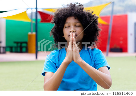 Tranquil biracial schoolgirl practicing yoga meditation in school playground, with copy space 116811400