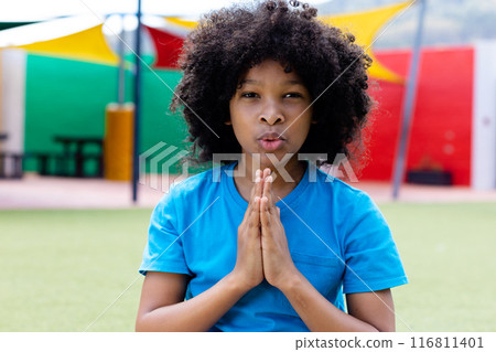Portrait of biracial schoolgirl practicing yoga meditation in school playground, with copy space 116811401