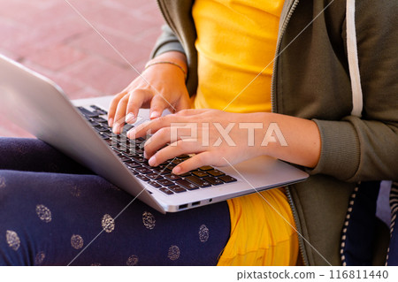 Midsection of caucasian schoolgirl using laptop, sitting outside school, with copy space 116811440
