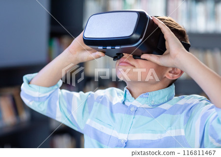 Caucasian schoolboy using vr headset in school library, with copy space 116811467