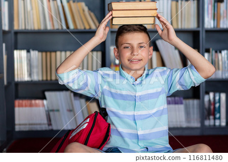 Smiling caucasian schoolboy with books on his head in library, copy space Smiling caucasian schoolboy with books on his head in library, copy space 116811480