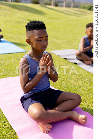 Happy african american schoolchildren doing yoga and meditating on field at school Happy african american schoolchildren doing yoga and meditating on field at school 116811541