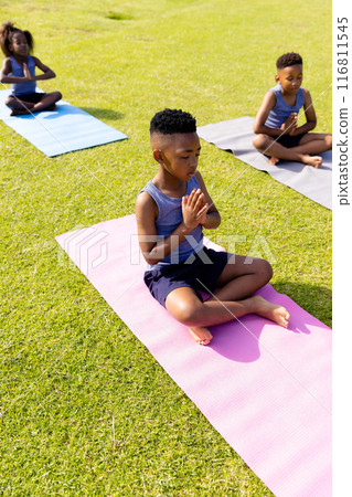 Happy african american schoolchildren doing yoga and meditating on field at school 116811545