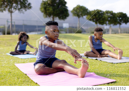 Happy african american schoolchildren doing yoga and stretching on field at school 116811552