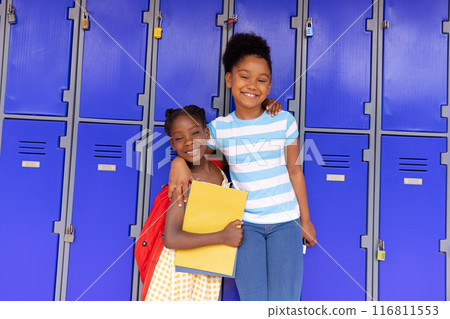 Portrait of happy african american schoolchildren standing next to locker in corridor at school 116811553
