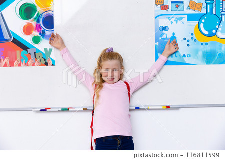 Portrait of happy caucasian schoolgirl in school classroom with chemistry posters in background Portrait of happy caucasian schoolgirl in school classroom with chemistry posters in background 116811599