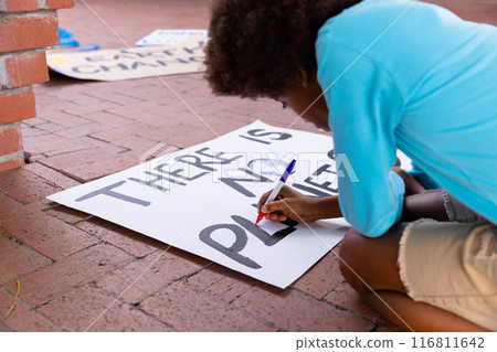 Happy african american schoolboy making ecology posters during outdoor school art class 116811642
