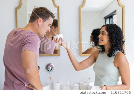 Smiling couple in bathroom, woman playfully holding skincare product to man's face Smiling couple in bathroom, woman playfully holding skincare product to man's face 116811706