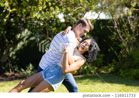 Young couple dancing and laughing together in sunny outdoor garden 116811733