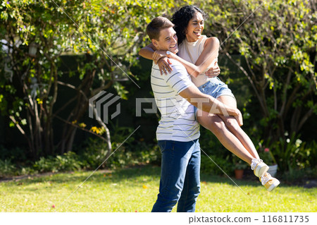 Man lifting and spinning woman in garden, both laughing and enjoying moment, copy space 116811735