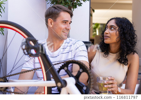 Young couple sitting together, holding drinks and talking near bicycle 116811797