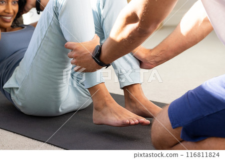 Assisting woman with exercise, man holding her legs on yoga mat Assisting woman with exercise, man holding her legs on yoga mat 116811824