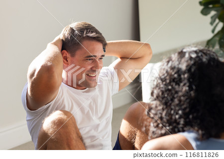 Smiling man doing sit-ups with partner during home workout session 116811826