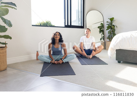 Practicing yoga together, young couple sitting on mats in bedroom, copy space 116811830