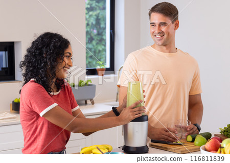 Making smoothies, young couple smiling and enjoying time together in kitchen Making smoothies, young couple smiling and enjoying time together in kitchen 116811839