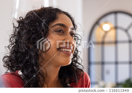 Smiling woman with curly hair looking away, enjoying moment indoors Smiling woman with curly hair looking away, enjoying moment indoors 116811849
