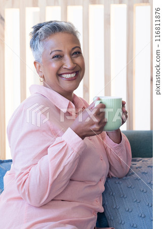 Smiling senior woman holding coffee mug, relaxing on couch at home 116811876