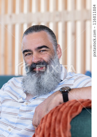 Smiling bearded senior man relaxing on couch, enjoying leisure time indoors 116811884