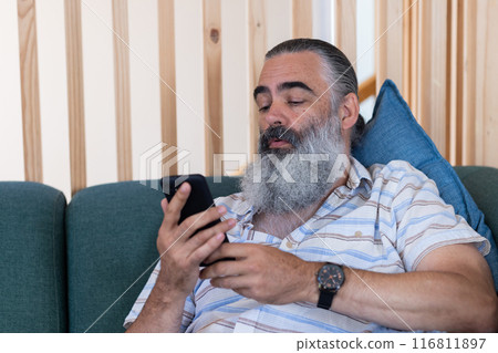 Using smartphone, bearded senior man relaxing on couch, checking messages 116811897