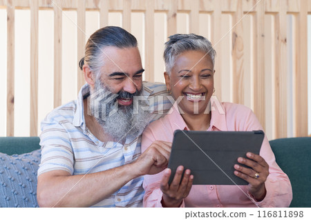 Smiling senior couple using tablet together while sitting on couch indoors 116811898