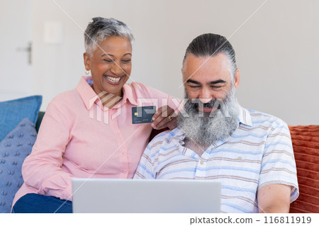 Using laptop and holding credit card, senior couple shopping online, smiling together Using laptop and holding credit card, senior couple shopping online, smiling together 116811919
