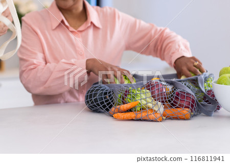 Unpacking fresh vegetables from reusable bag, person organizing groceries in kitchen 116811941