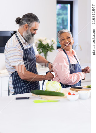 Senior couple in kitchen, man tying apron on woman, preparing to cook together Senior couple in kitchen, man tying apron on woman, preparing to cook together 116811947