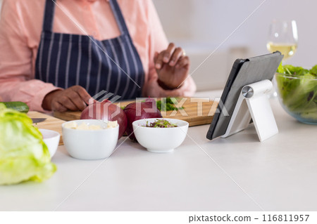 Chopping vegetables, person following recipe on tablet in modern kitchen Chopping vegetables, person following recipe on tablet in modern kitchen 116811957