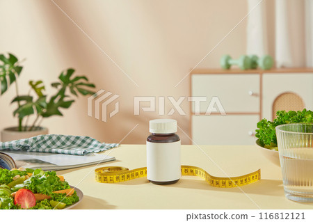 Mockup for advertising losing weight drugs was taken from front. A drug bottle without label displayed in center with a yellow measuring tape decorated in back, dietary food placed on both sides 116812121