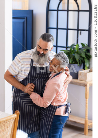 Wearing aprons, senior couple dancing together in cozy kitchen Wearing aprons, senior couple dancing together in cozy kitchen 116812168