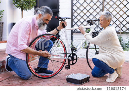 Repairing bicycle together, senior couple enjoying outdoor activity in courtyard 116812174