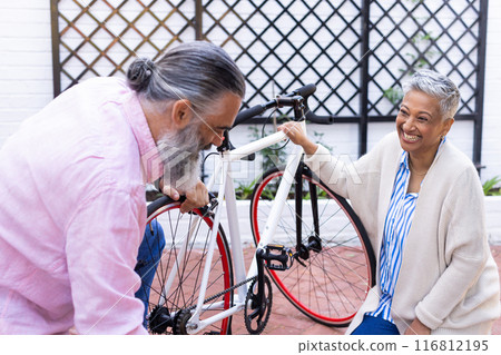 Fixing bicycle, senior couple enjoying outdoor activity together, smiling and bonding 116812195