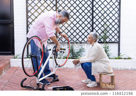 Repairing bicycle, senior man fixing bike while woman sitting and watching Repairing bicycle, senior man fixing bike while woman sitting and watching 116812198