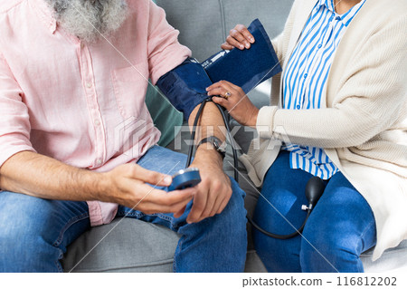 Checking blood pressure, woman assisting senior man with medical device on couch Checking blood pressure, woman assisting senior man with medical device on couch 116812202